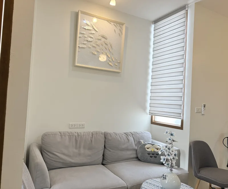 The upstairs waiting corner, with a grey sofa, an owl cushion and a window